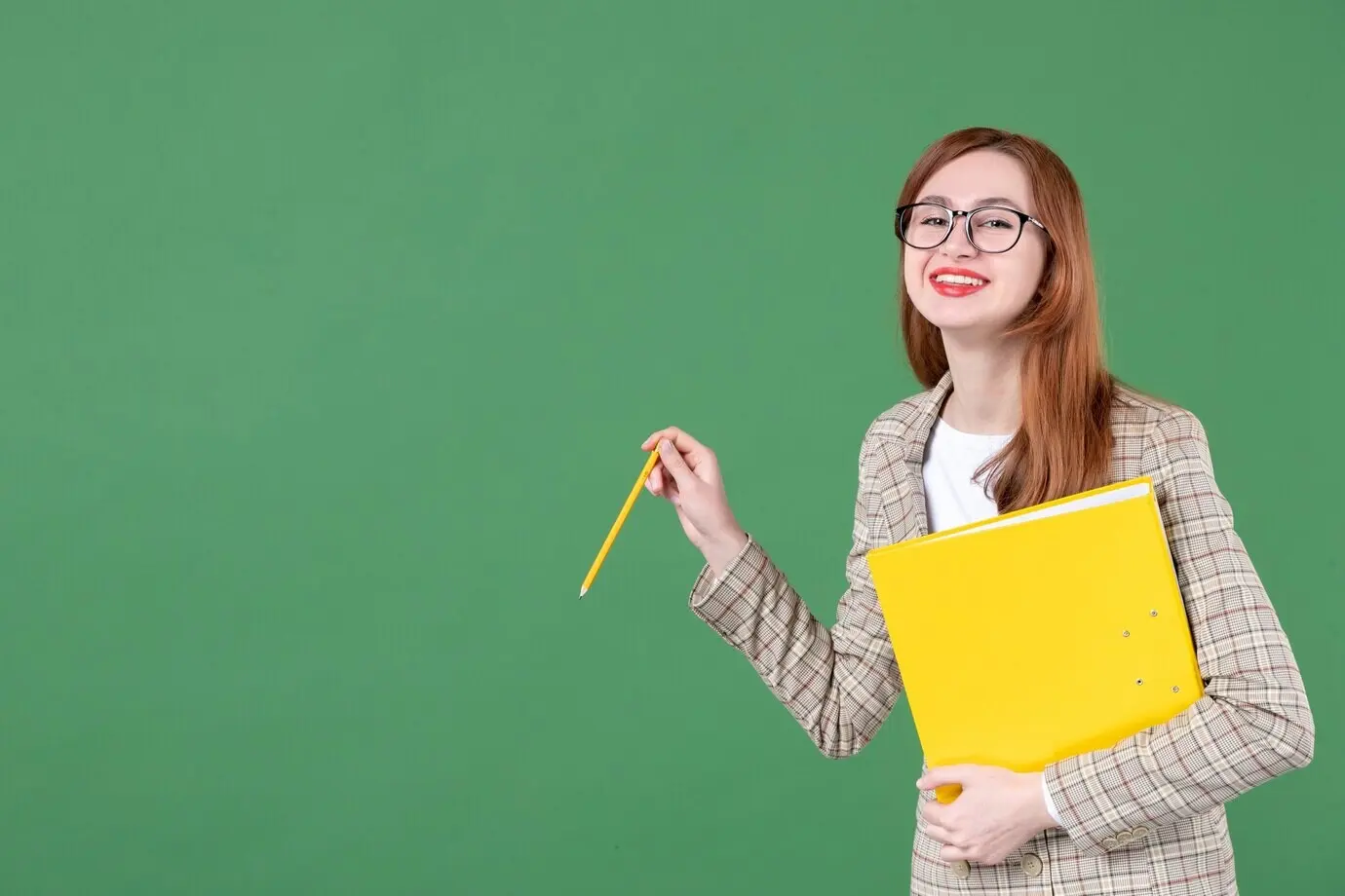 Porträt einer Lehrerin, die ein gelbes Dokument hält und vor grünem Hintergrund lächelt.