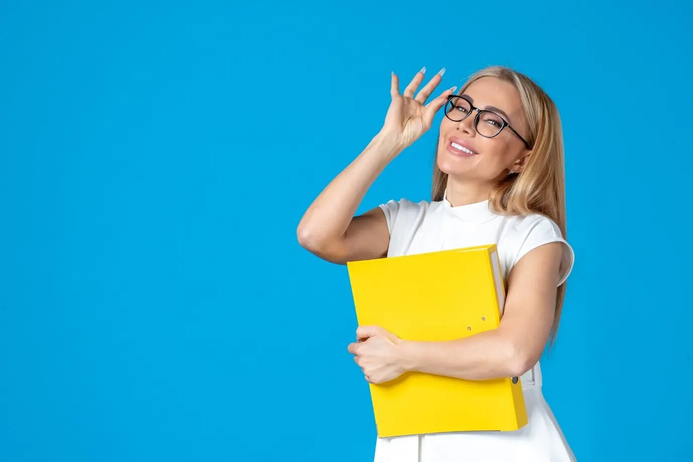 Frontalansicht einer weiblichen Mitarbeiterin in weißem Kleid, die eine gelbe Mappe hält, vor blauer Wand.